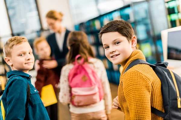 Adorables écoliers avec sacs à dos regardant la caméra dans la bibliothèque — Photo de stock