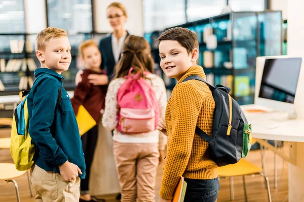 Schoolboys with books and backpacks looking at camera in library — Stock Photo