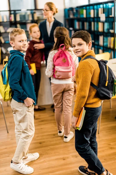 Jungen mit Büchern und Rucksäcken blicken in Bibliothek in die Kamera — Stockfoto