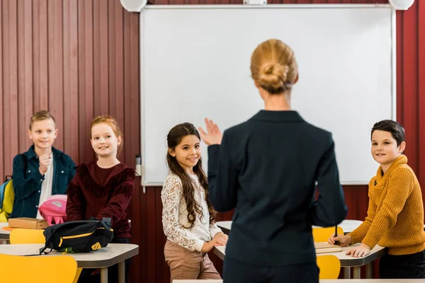 Vue arrière du jeune professeur parlant avec des écoliers souriants — Photo de stock