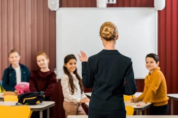 Back view of teacher talking with smiling schoolchildren — Stock Photo