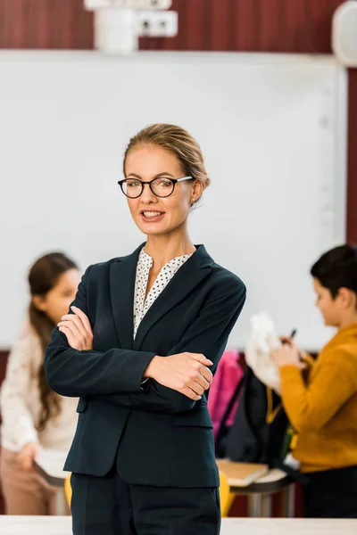 Junge Lehrerin mit Brille lächelt in die Kamera, während Schüler hinter ihr stehen — Stockfoto