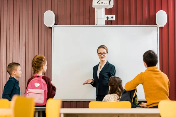 Junge Lehrerin präsentiert süße Schulkinder mit Rucksack — Stockfoto