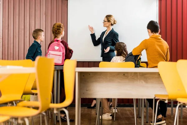 Schoolchildren with backpacks looking at teacher showing at interactive whiteboard — Stock Photo