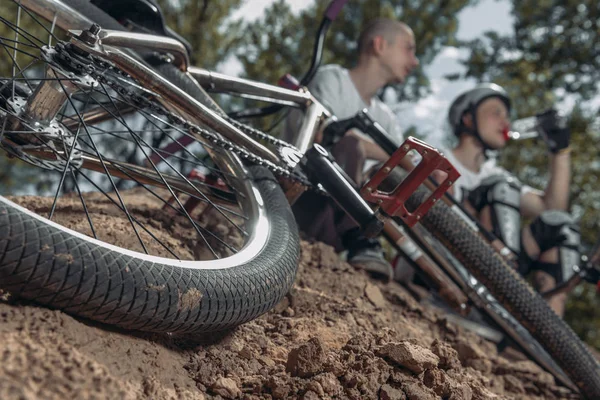 Two bikers resting and drinking water with bike on foreground — Stock Photo