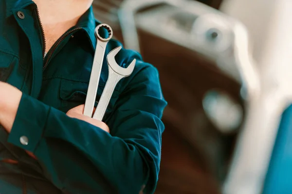 Cropped shot of auto mechanic in overall holding wrench and ring spanner — Stock Photo