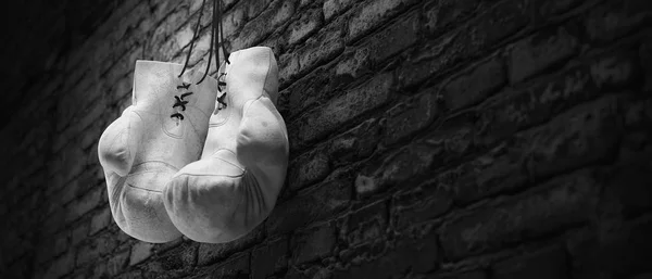 Old white boxing gloves hang on nail on brick wall with copy space for text. High resolution 3d render