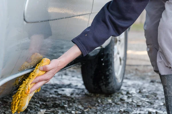 The man washes with a sponge with foam the car. To wash the car on the street in the spring. To rinse with soap water the car and wheels