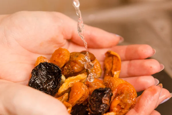 The girl washes dry fruit with water. Dry fruit in hands.