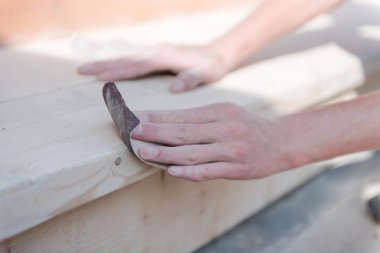 Tahtayı zımpara kağıdıyla zımparala. Bir adam bir ağacı parlatır. Zımpara kağıdıyla çalış. Ahşap ürünler yapmak için. Tahtaları yumuşak yap.