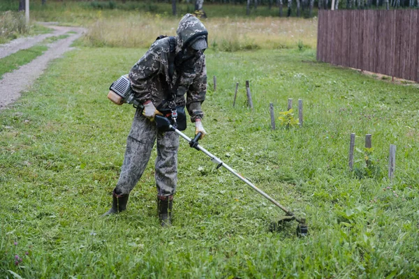 The man is mowing the grass. Cut the grass with a trimmer. The man is cleaning the garden. Occupation. Agriculture. Cleaning of the territory. Cut the lawn