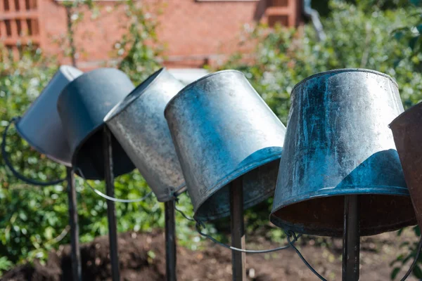 Metal buckets in the garden. Water from a bucket. The bucket weighs on the fence. Tools in the garden. Agriculture. Old buckets. Village life