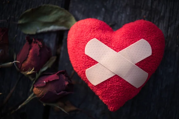 First Aid Band Cushioned Plaster Strip Medical Patch glued on red heart with dried red rose on wooden background. Heart broken, Love and Valentines day concept.