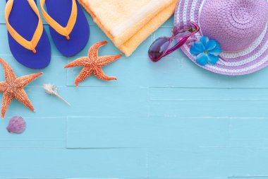 Plaj aksesuarları, güneş gözlüğü, deniz yıldızı, şapka plaj, sarı havlu da dahil olmak üzere mavi renkli flip flop ve kabuk üzerinde parlak pastel ahşap arka plan yaz tatil ve tatil konsepti için.