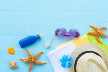 Mavi plaj aksesuarları, güneş gözlüğü, Güneş kremi denizyıldızı, şapka beach de dahil olmak üzere havlu, renkli flip flop ve kabuk üzerinde parlak pastel ahşap arka plan yaz tatil ve tatil konsepti için.