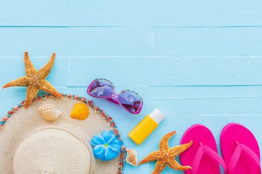 Plaj aksesuarları, güneş gözlüğü, deniz yıldızı, şapka plaj da dahil olmak üzere güneş kremi, renkli flip flop ve kabuk üzerinde parlak pastel ahşap arka plan için mavi yaz tatil ve tatil kavramı.