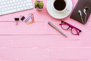 Üstten görünüm ofis masası çalışma alanı ve ofis aksesuarları dahil olmak üzere klavye, Gözlük, klipler, çiçek, kalem, Not defteri, kulaklık ve kahve pembe ahşap arka plan ile.
