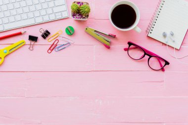 Üstten görünüm ofis masası çalışma alanı ve ofis aksesuarları dahil olmak üzere klavye, Gözlük, klipler, çiçek, kalem, Not defteri, kulaklık ve kahve pembe ahşap arka plan ile.