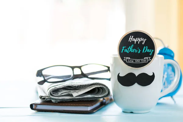Happy fathers day concept. coffee cup with black paper mustache, heart tag with  Happy father\'s day text and newspaper, glasses on wooden table background.