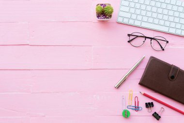 Üstten görünüm Ofis masaları dahil olmak üzere klavye, Gözlük, klipler, çiçek, kalem, Not defteri, belge ve kahve pembe ahşap arka plan üzerinde kırpma çalışma alanı ve ofis aksesuarları ile.
