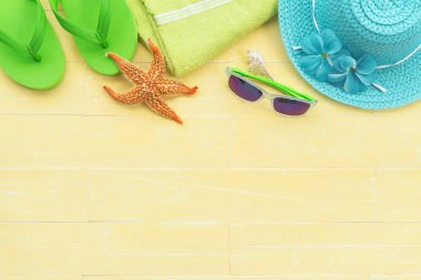 Plaj aksesuarları, güneş gözlüğü, deniz yıldızı, şapka plaj da dahil olmak üzere retro kamera, yeşil havlu, renkli flip flop ve deniz kabuğu parlak sarı pastel ahşap arka plan üzerinde yaz tatil ve tatil konsepti için.