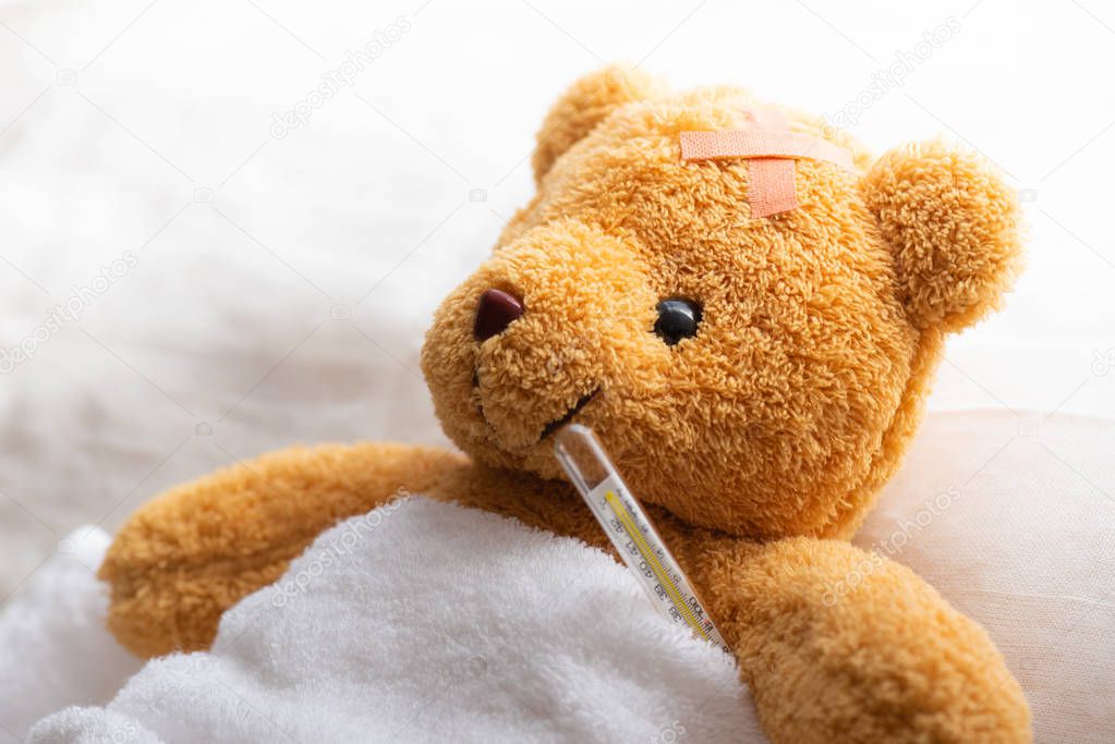 Teddy bear lying sick in hospital bed with with thermometer and plaster. Healthcare and medical concept.