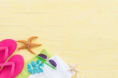 Plaj aksesuarları, güneş gözlüğü, deniz yıldızı, şapka plaj, yeşil havlu da dahil olmak üzere renkli flip flop ve deniz kabuğu üzerinde parlak sarı pastel ahşap arka plan yaz tatil ve tatil konsepti için.