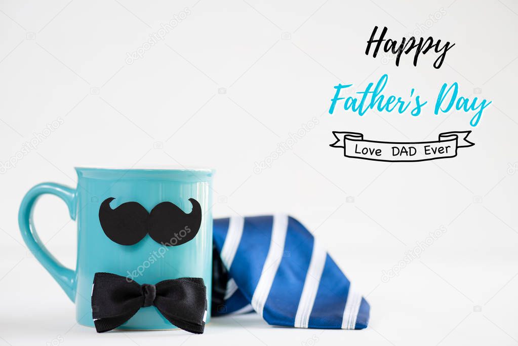 Happy fathers day concept. blue tie with mustache and bow tie on cyan pastel coffee cup on bright white wooden table background.