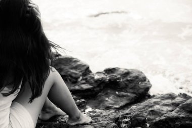 Yalnız plajda, üzgün kavramı bir kayaya oturan üzgün kadın arkadan görünüm. Siyah ve beyaz fotoğraf.