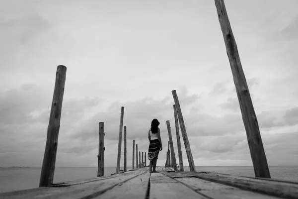 Black and white of Sad and lonely woman stand alone on a the wooden bridge over the sea