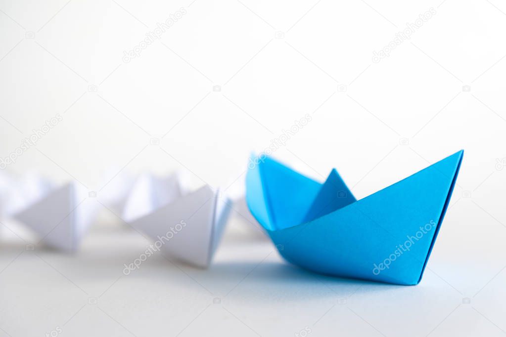 Leadership concept. blue paper ship lead among white. One leader ship leads other ships.