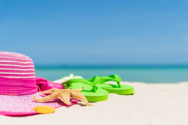 Plaj aksesuarları dahil olmak üzere flip flop, deniz yıldızı, plaj şapka ve deniz kabuğu kumsalı, yeşil deniz ve mavi gökyüzü arka plan üzerinde yaz tatil ve tatil konsepti için.