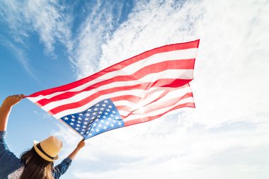 Amerika Birleşik Devletleri bayrağı tutarak ve koşma, mavi gökyüzü ile kollarını açarak kaygısız atlama genç mutlu kadın kapatın. ABD Bağımsızlık günü, 4 Temmuz.