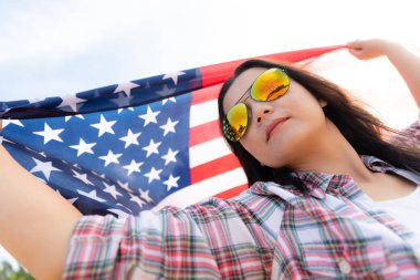 Amerika Birleşik Devletleri bayrağı tutarak ve kumsalda kollarını açarak kaygısız çalışan mutlu kadın kapatın. ABD Bağımsızlık günü kavramı.