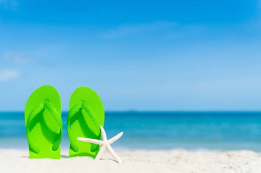 yeşil flip flop ile denizyıldızı kumsalı, yeşil deniz ve mavi gökyüzü arka plan üzerinde yaz tatil ve tatil konsepti için.