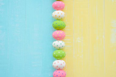 Mutlu Paskalyalar! Parlak mavi ve sarı ahşap arka plan üzerinde renkli kağıt çiçeklerle satır Paskalya yumurtaları.
