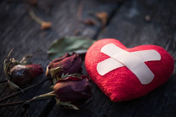 First Aid Band Cushioned Plaster Strip Medical Patch glued on red heart with dried red rose on wooden background. Heart broken, Love and Valentines day concept.