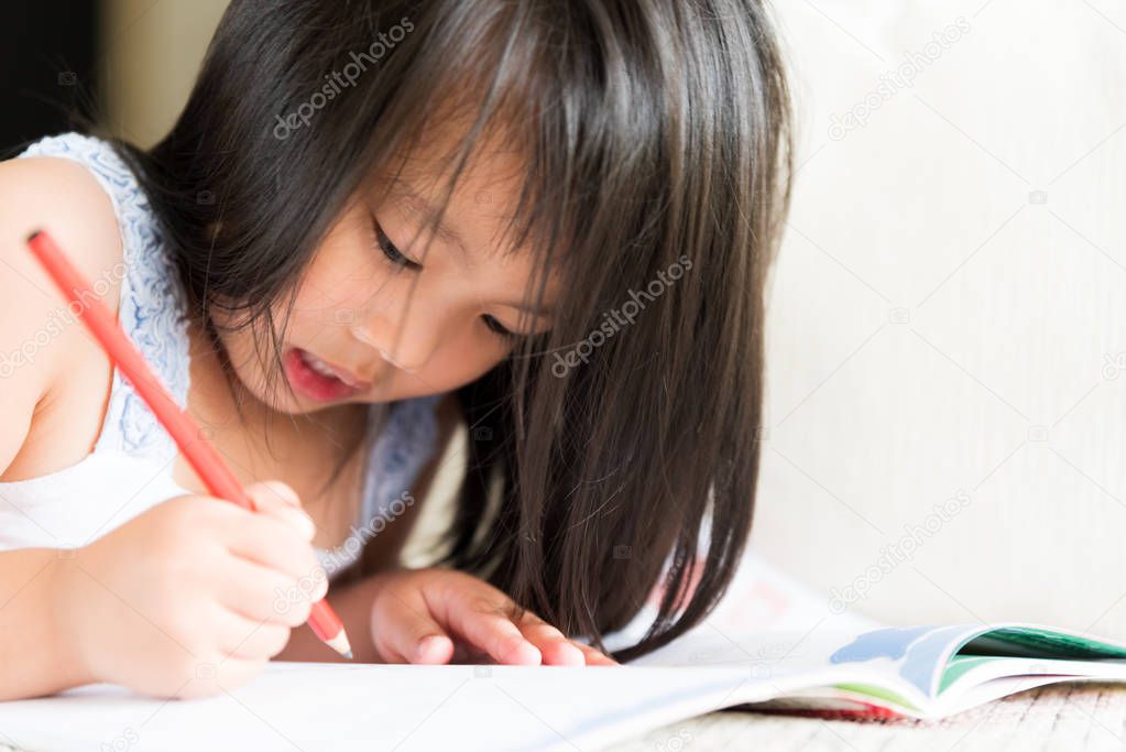 Happy cute little girl smiling and holding red pencil and drawing, writing on a book to do homework.