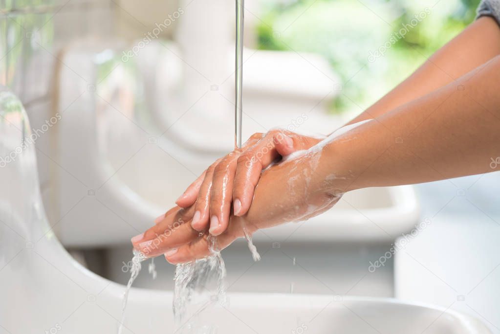 Closeup woman washing hands with soap under the faucet with water  in the bathroom.