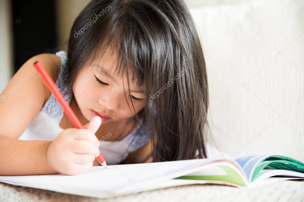 Happy cute little girl smiling and holding red pencil and drawing, writing on a book to do homework.