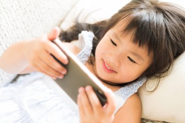 Sevimli küçük kız koltukta yalan akıllı telefon üzerinde oyun oynamak için eğlenceli olması.