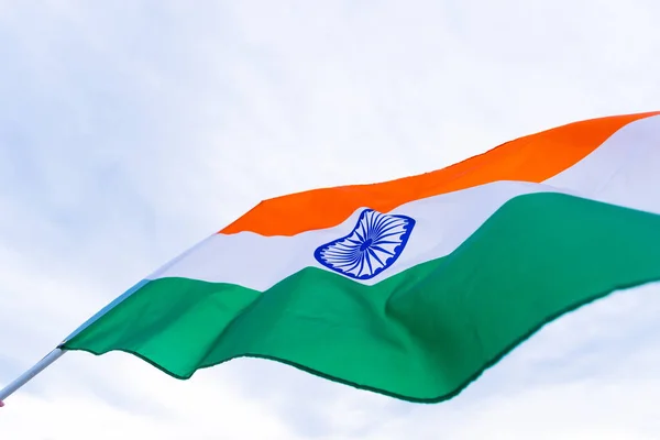 Close up man hand holding India flag on the blue sky background. Indian Independence Day, 15 August.