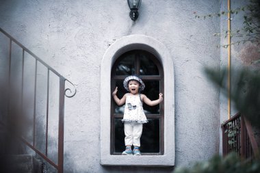 Gülümseyen ve vintage renk tonu ile cam kenarında duran mutlu sevimli küçük kız.