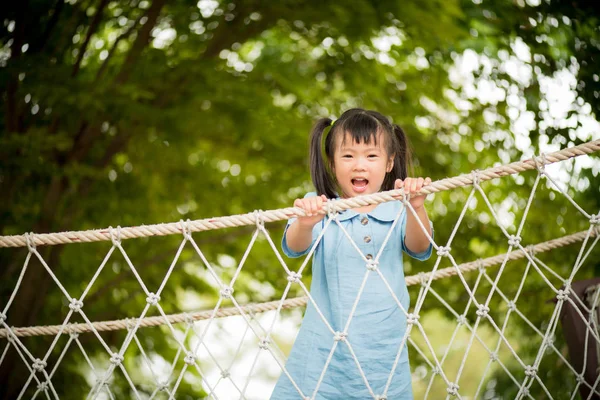 暑い夏の日に冒険公園カラフルな庭のロープの橋に登って遊んで幸せな女の子 子供のための夏の活動 — ストック写真