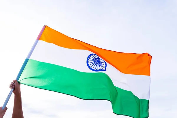 Close up man hand holding India flag on the blue sky background. Indian Independence Day, 15 August.