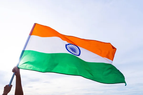 Close up man hand holding India flag on the blue sky background. Indian Independence Day, 15 August.