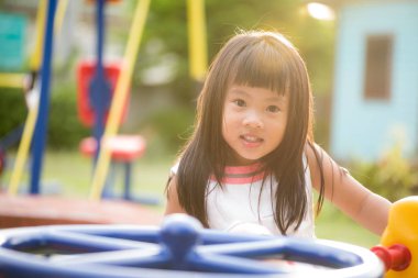 Sıcak bir yaz günü güneşli Şehir parkındaki bir salıncak yolculuk zevk Bahçesi eğleniyor mutlu küçük kız.