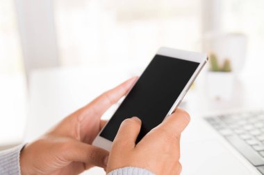 Ofiste bir dizüstü bilgisayar ile bir masada beyaz cep telefonu tutan kadın el.