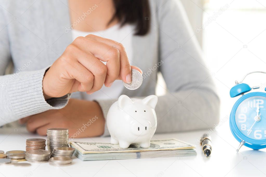 Woman hand holding piggy bank with stack of coins and America dollars banknotes on table. Saving money wealth and financial concept.