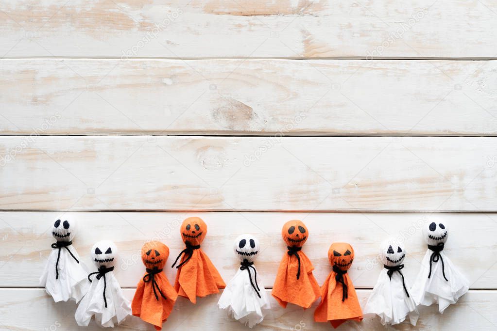 Top view of Halloween crafts, white and orange paper ghost on white wooden background with copy space for text. halloween concept.